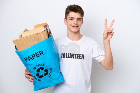 Téléchargez les photos : Adolescent homme russe tenant un sac de recyclage plein de papier pour recycler isolé sur fond blanc souriant et montrant signe de victoire - en image libre de droit