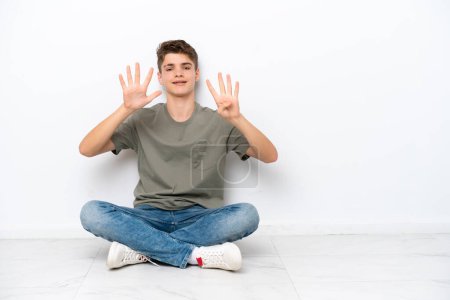 Foto de Adolescente ruso hombre sentado en el suelo aislado sobre fondo blanco contando nueve con los dedos - Imagen libre de derechos