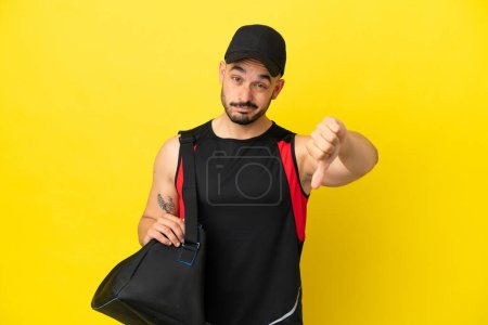 Photo for Young sport caucasian man with sport bag isolated on yellow background showing thumb down with negative expression - Royalty Free Image
