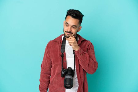 Téléchargez les photos : Jeune photographe homme caucasien isolé sur fond bleu regardant sur le côté - en image libre de droit