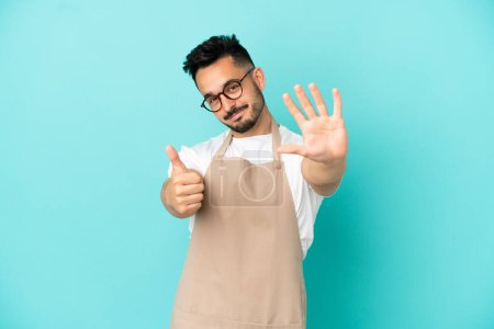 Téléchargez les photos : Serveur restaurant homme caucasien isolé sur fond bleu comptant six avec les doigts - en image libre de droit