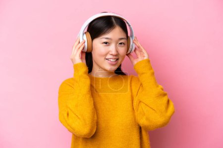 Téléchargez les photos : Jeune femme chinoise isolée sur fond rose écoutant de la musique - en image libre de droit