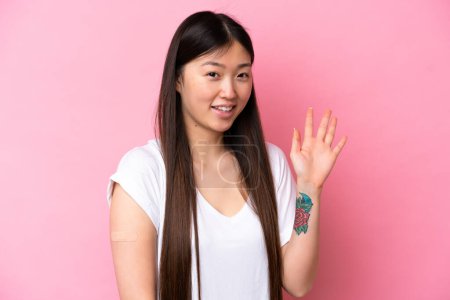 Junge Chinesin mit Band auf rosa Hintergrund salutiert mit fröhlichem Gesichtsausdruck