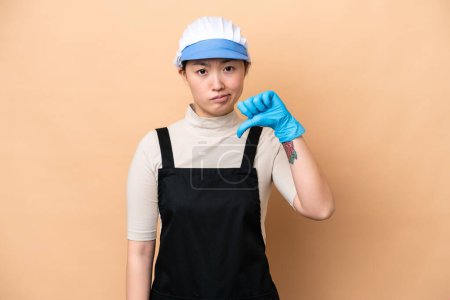 Photo for Young Chinese Fishmonger woman wearing an apron and holding a raw fish isolated on pink background showing thumb down with negative expression - Royalty Free Image