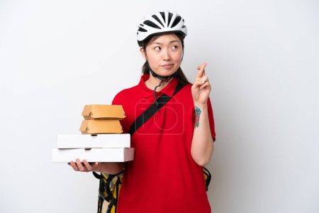Photo for Young Chinese delivery woman taking takeaway food isolated on white background with fingers crossing and wishing the best - Royalty Free Image