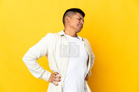 Foto de Joven ecuatoriano aislado sobre fondo amarillo sufriendo de dolor de espalda por haber hecho un esfuerzo - Imagen libre de derechos