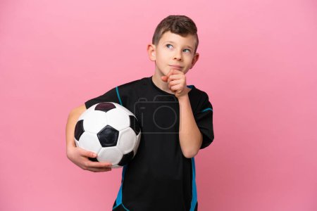 Téléchargez les photos : Petit joueur de football caucasien garçon isolé sur fond rose et regardant vers le haut - en image libre de droit