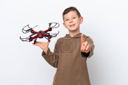 Foto de Pequeño chico caucásico sosteniendo un dron aislado sobre fondo blanco mostrando y levantando un dedo - Imagen libre de derechos