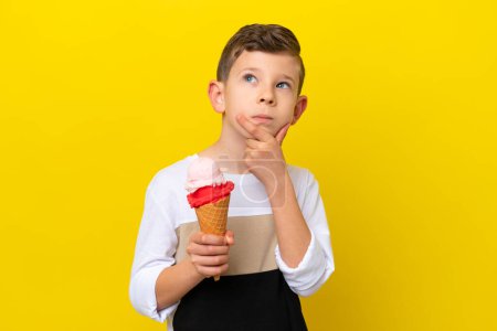 Foto de Pequeño chico caucásico con un helado de corneta aislado sobre fondo amarillo que tiene dudas - Imagen libre de derechos