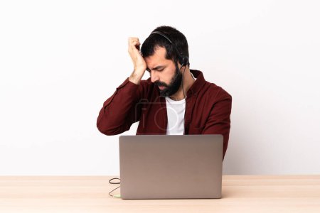 Photo for Telemarketer caucasian man working with a headset and with laptop with headache. - Royalty Free Image