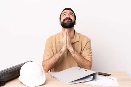 Photo for Caucasian architect man with beard in a table keeps palm together. Person asks for something. - Royalty Free Image