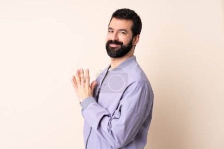 Kaukasischer Mann mit Bart, der eine Jacke über isoliertem Hintergrund trägt und etwas intrigiert