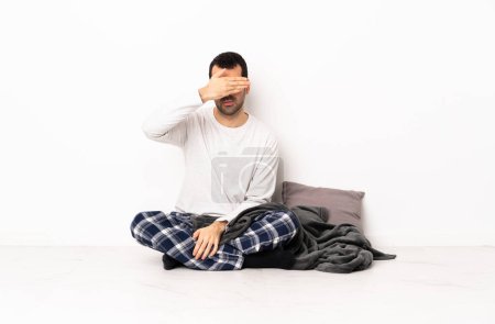 Foto de Hombre caucásico en pijama sentado en el suelo en el interior cubriendo los ojos con las manos. No quiero ver algo. - Imagen libre de derechos