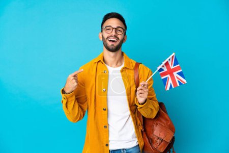 Téléchargez les photos : Jeune homme caucasien tenant un drapeau du Royaume-Uni isolé sur fond jaune donnant un geste pouce levé - en image libre de droit