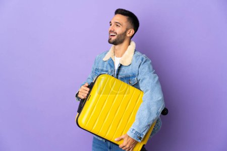 Photo for Young caucasian man isolated on blue background in vacation with travel suitcase - Royalty Free Image