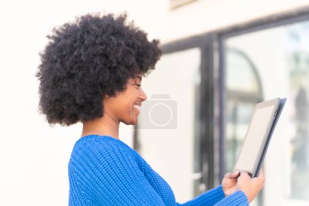 Téléchargez les photos : Afro-américaine fille tenant une tablette à l'extérieur avec expression heureuse - en image libre de droit