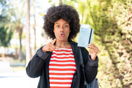 Téléchargez les photos : Afro-américaine fille tenant un passeport à l'extérieur surpris et pointant devant - en image libre de droit