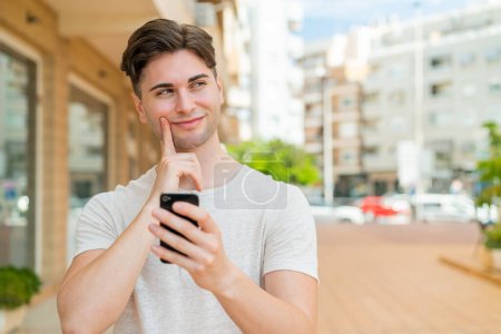 Téléchargez les photos : Jeune homme beau utilisant le téléphone mobile et la pensée - en image libre de droit