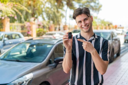 Photo for Young handsome man holding car keys at outdoors and pointing it - Royalty Free Image