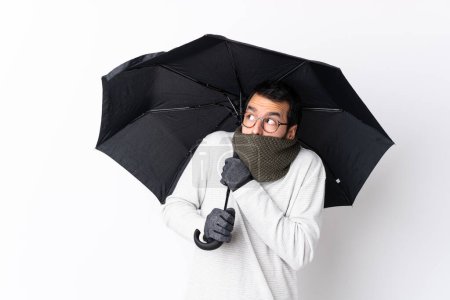 Téléchargez les photos : Homme beau caucasien avec barbe tenant un parapluie sur mur blanc isolé - en image libre de droit