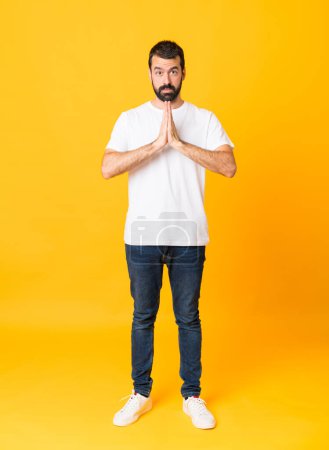 Photo for Full-length shot of man with beard over isolated yellow background keeps palm together. Person asks for something - Royalty Free Image