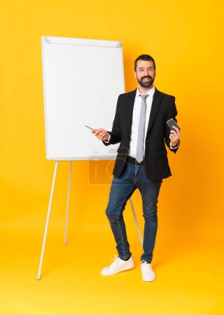 Photo for Full-length shot of businessman giving a presentation on white board over isolated yellow background - Royalty Free Image