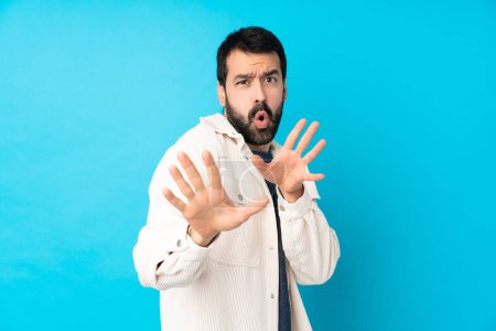 Foto de Joven hombre guapo con chaqueta de pana blanca sobre fondo azul aislado manos nerviosas estiramiento en la parte delantera - Imagen libre de derechos