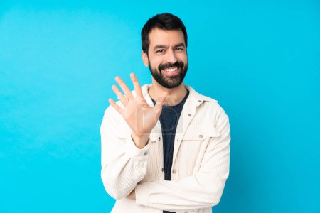 Photo for Young handsome man with white corduroy jacket over isolated blue background counting five with fingers - Royalty Free Image