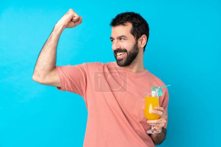 Téléchargez les photos : Jeune homme tenant un cocktail sur fond bleu isolé célébrant une victoire - en image libre de droit