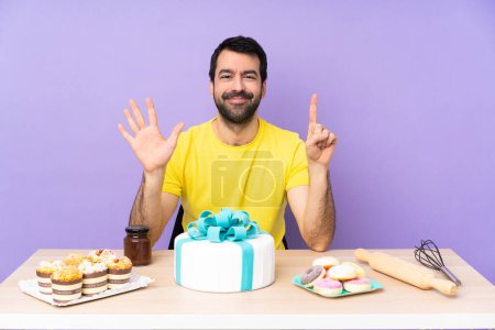 Téléchargez les photos : Homme dans une table avec un gros gâteau comptant six avec des doigts - en image libre de droit