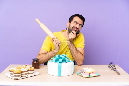 Téléchargez les photos : Homme dans une table avec un gros gâteau sur fond violet - en image libre de droit