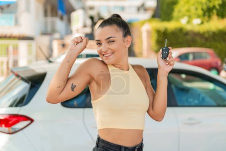 Téléchargez les photos : Jeune jolie femme à l'extérieur tenant des clés de voiture et célébrant une victoire - en image libre de droit