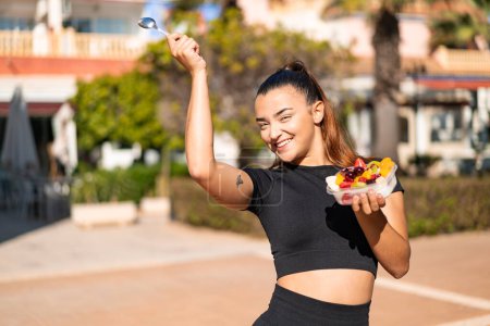 Téléchargez les photos : Jeune jolie femme brune tenant un bol de fruits à l'extérieur - en image libre de droit