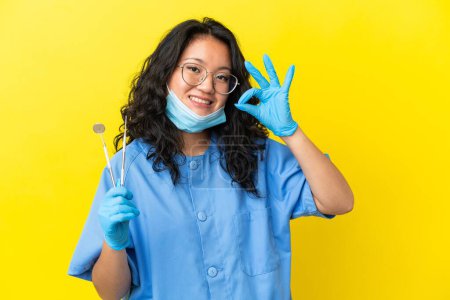 Foto de Joven asiático dentista holding herramientas sobre aislado fondo mostrando ok signo con los dedos - Imagen libre de derechos