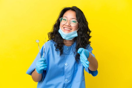 Foto de Joven asiático dentista sosteniendo herramientas sobre aislado fondo apretando manos para cerrar un buen negocio - Imagen libre de derechos