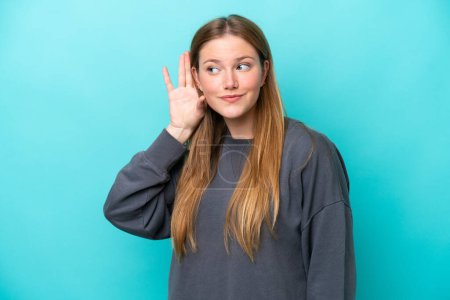 Photo for Young caucasian woman isolated on blue background listening to something by putting hand on the ear - Royalty Free Image