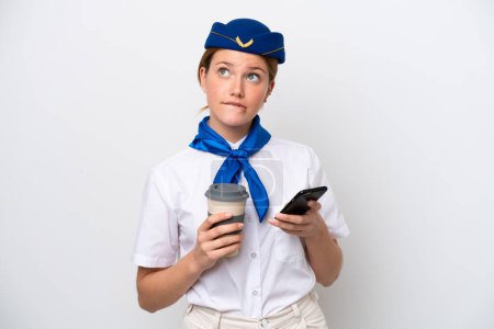Téléchargez les photos : Hôtesse de l'air femme isolée sur fond blanc tenant café à emporter et un mobile tout en pensant quelque chose - en image libre de droit