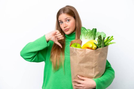 Photo for Young caucasian woman holding a grocery shopping bag isolated on white background showing thumb down with negative expression - Royalty Free Image