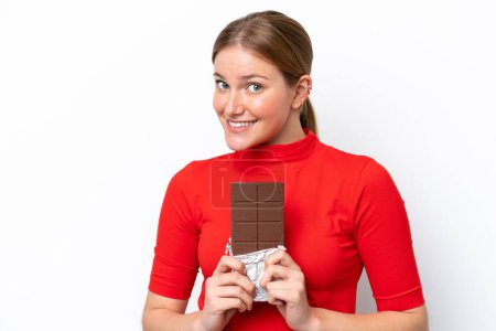 Jeune femme caucasienne isolée sur fond blanc prenant une tablette de chocolat et heureuse