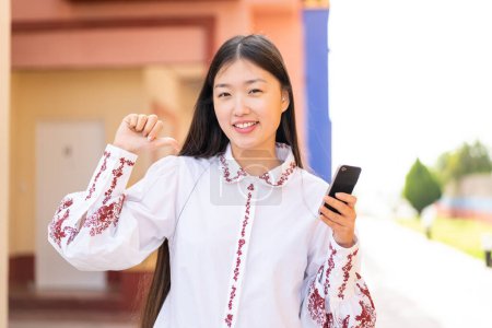Téléchargez les photos : Jeune femme chinoise utilisant un téléphone mobile à l'extérieur fier et satisfait de soi - en image libre de droit