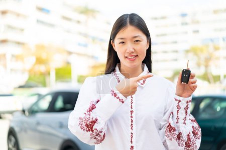 Foto de Joven mujer china sosteniendo las llaves del coche al aire libre y señalándolo - Imagen libre de derechos