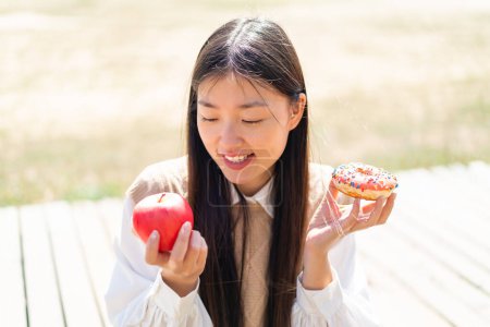Téléchargez les photos : Jeune femme chinoise à l'extérieur tenant pomme et beignet avec expression heureuse - en image libre de droit