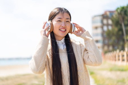 Téléchargez les photos : Jeune femme chinoise à l'extérieur écouter de la musique - en image libre de droit