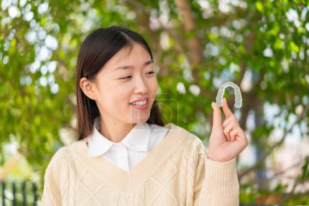 Foto de Joven mujer china sosteniendo frenos invisibles al aire libre con expresión feliz - Imagen libre de derechos