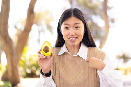 Photo for Pretty Chinese woman holding an avocado at outdoors with surprise facial expression - Royalty Free Image