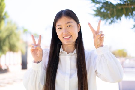 Photo for Pretty Chinese woman at outdoors showing victory sign with both hands - Royalty Free Image