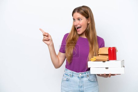Téléchargez les photos : Jeune jolie femme blonde tenant fast food isolé sur fond blanc pointant du doigt vers le côté et présentant un produit - en image libre de droit