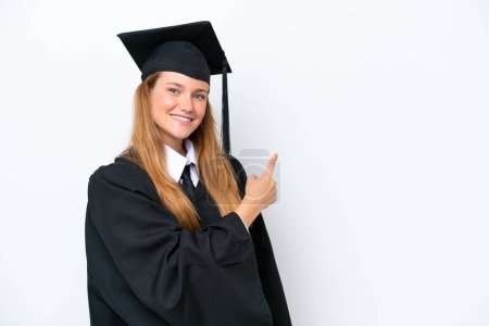 Téléchargez les photos : Jeune diplômée universitaire caucasienne isolée sur fond blanc pointant vers le côté pour présenter un produit - en image libre de droit