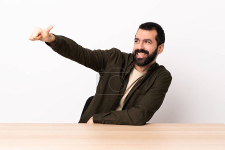 Foto de Caucásico hombre con barba en una mesa dando un gesto pulgar hacia arriba. - Imagen libre de derechos