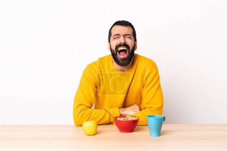 Foto de Hombre caucásico desayunando en una mesa gritando al frente con la boca abierta. - Imagen libre de derechos